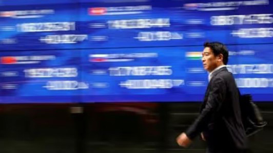 A passerby walks past an electric monitor displaying various countries' stock price index outside a bank in Tokyo, Japan. (Reuters Photo)